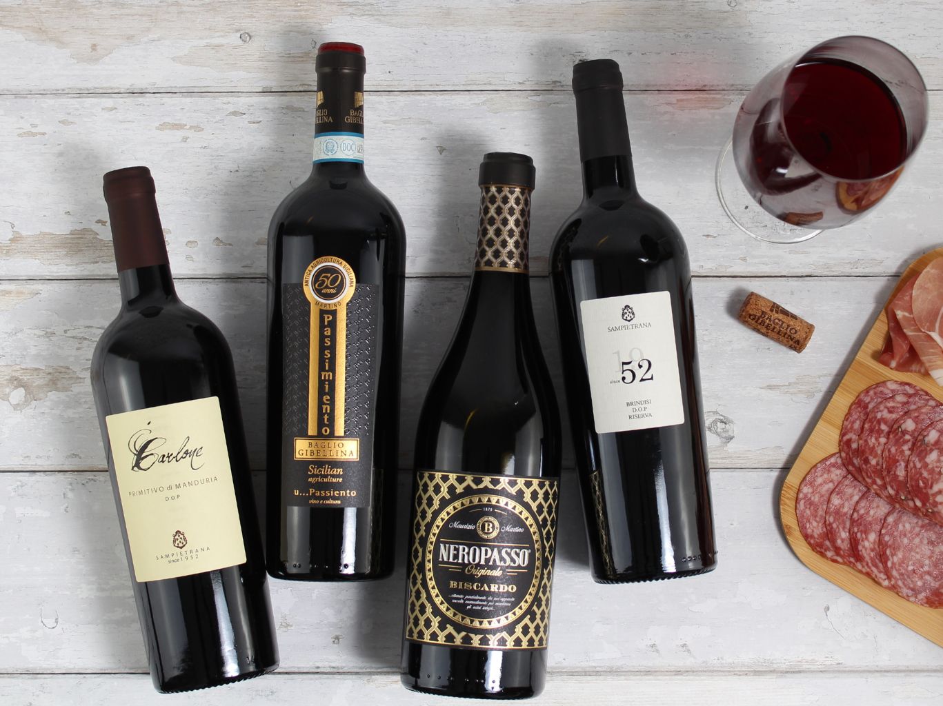Italian red wines lay down on silver grey wooden floor alongside an antipasti platter or charcuterie and a glass of red wine