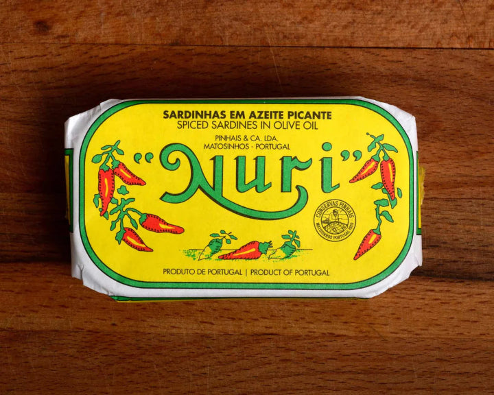 Packaged spiced sardines with 'Nuri' branding on a wooden surface