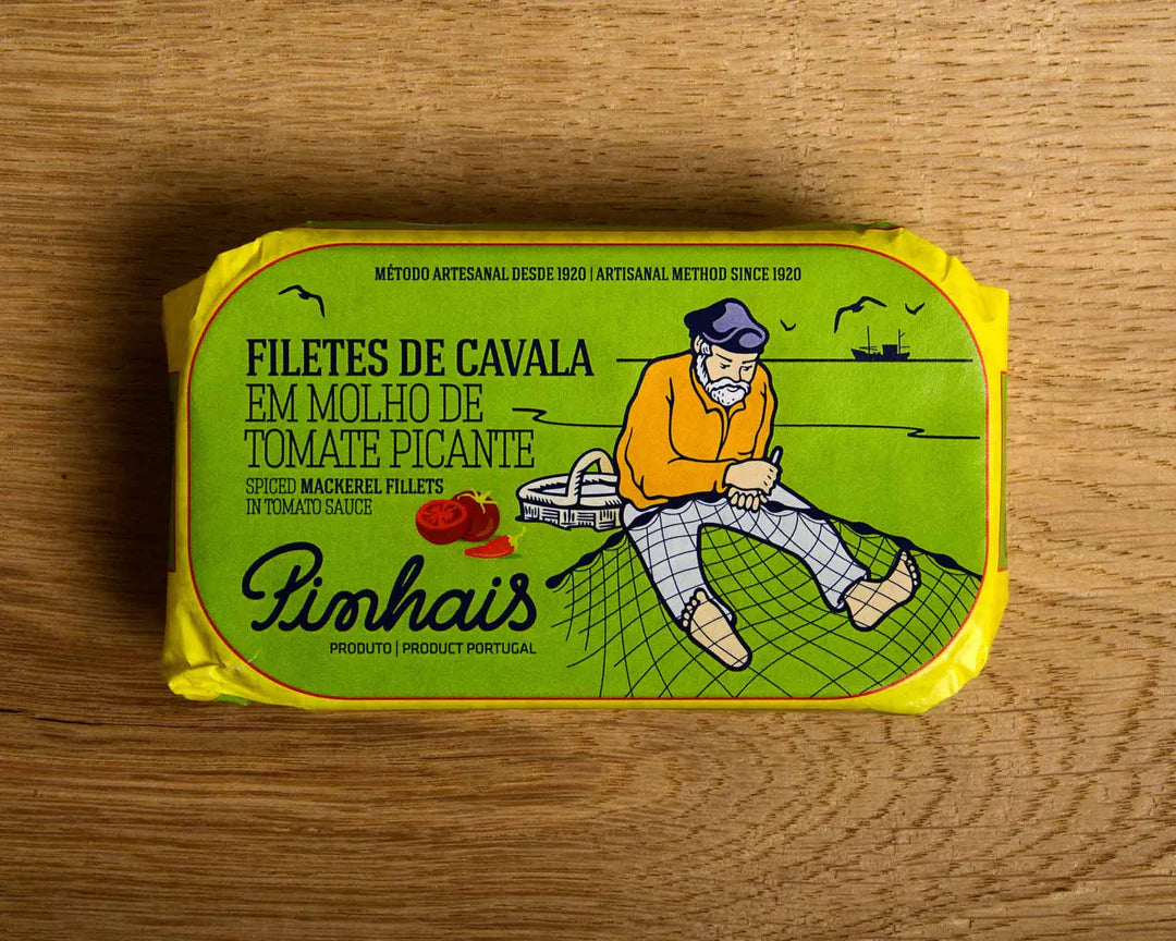 Pinhais Mackerel fillets in tomato sauce with a green label featuring an illustration of a fisherman on a wooden surface