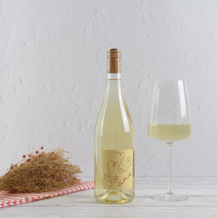 Bottle of Amie Blanc Sauvignon Blanc white wine with a glass on a textured white background