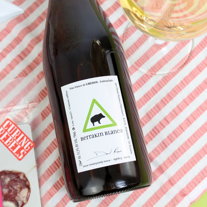 Bottle of Berrakin Blanco wine with a glass on a striped pink and white background