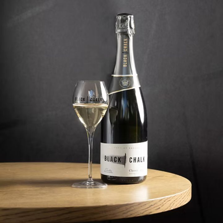 Bottle and glass of Black Chalk English Sparkling wine on a wooden surface with a dark background