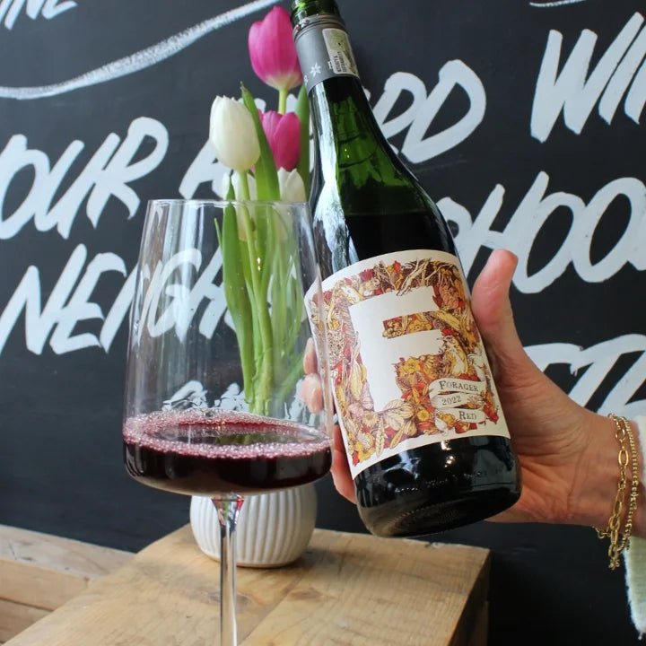 Forage red with a glass poured in West Didsbury Reserve in front of a blackboard with chalk writing.