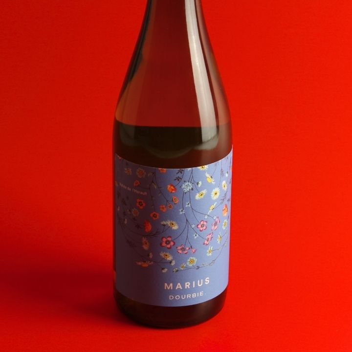 A bottle of La Dourbie, Marius Blanc 2024 floral label, set against a solid red background.