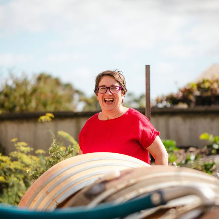 KATE MCINTYRE MW wearing a red shirt with a winery hose and barrels in the foreground