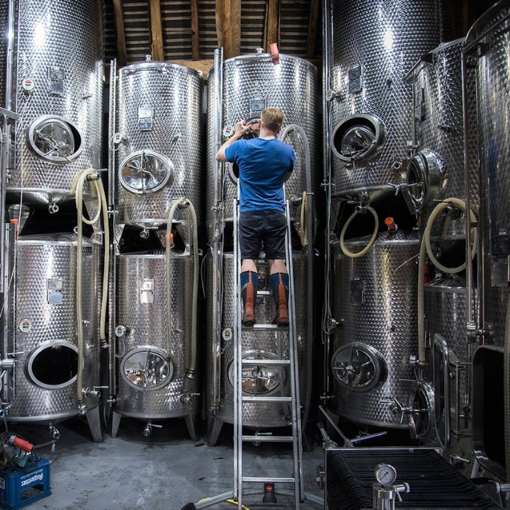 A Mountfield worker on a ladder among large metallic wine tanks in a winery.