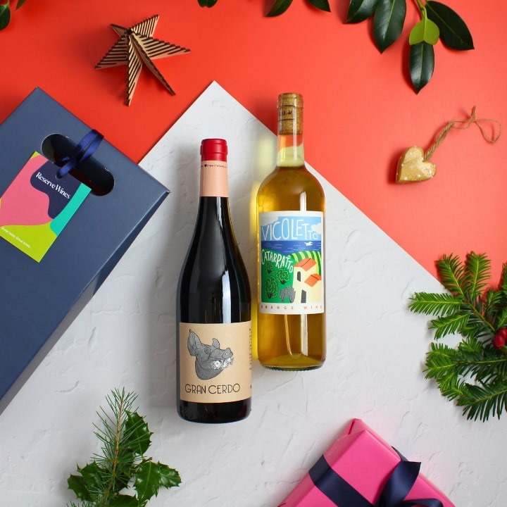 Two wine bottles on a white surface with Christmas decorations and gift boxes.