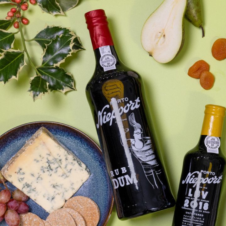 Two bottles of Niepoort Port wine with a plate of cheese, grapes, and pears on a green background.