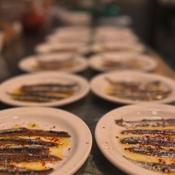 Several small white plates holding grilled fish on a dark table, photographed with a shallow depth of field that blurs the background and foreground plates.