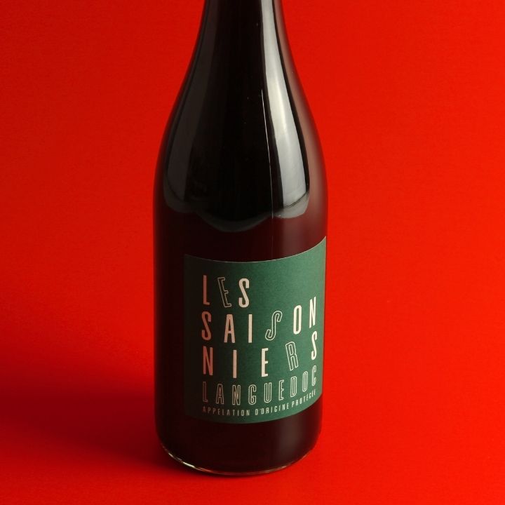 A dark glass bottle of Languedoc wine with a green label reading 'LES SAISONNIERS' against a solid red background.