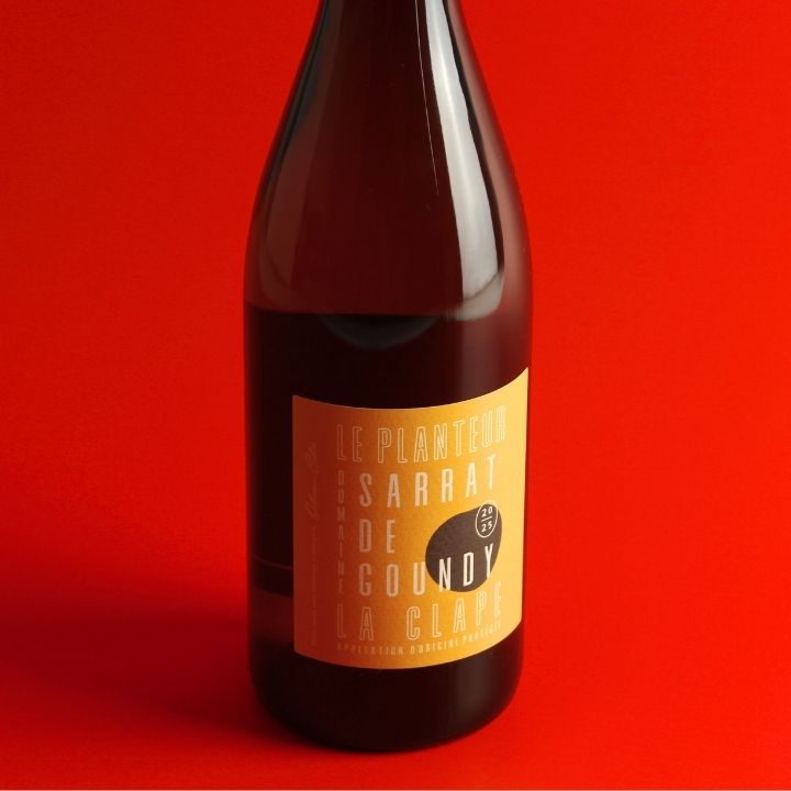 A dark brown glass bottle of Sarrat de Goundy, Le Planteur Blanc 2025 La Clave sparkling wine, featuring a mustard yellow label with black text, set against a solid red background.