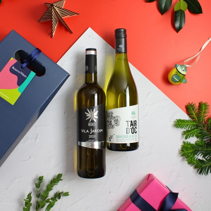 Two wine bottles on a white surface with decorative elements including a gift box and Christmas decorations.