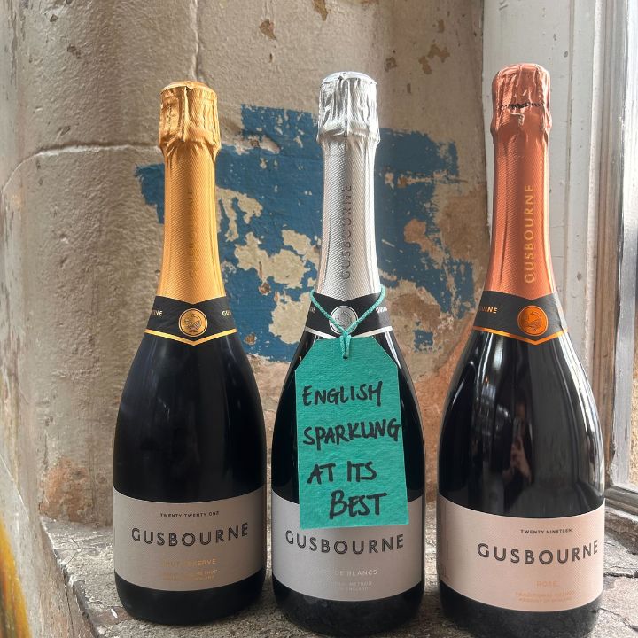 Three Gusbourne sparkling wine bottles against a textured wall.